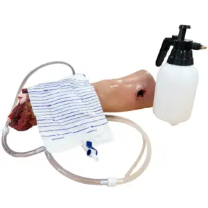 A simulated traumatic arm training model connected to tubing and a fluid bag beside a white spray bottle.